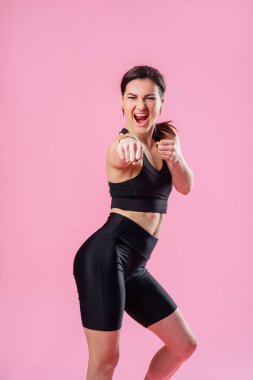 Sıska kadın havayı tekmeliyor, elleri ve bacakları havada. Atletik kız boks egzersizleri yapıyor, direkt vuruş yapıyor. Pembe arka planda izole edilmiş genç bir kızın fotoğrafı. Kuvvet ve motivasyon.
