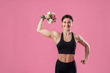 Çekici bir kız. Kaslı ve çok güzel bir vücudu var. Elinde pembe şakayık çiçekleri var. Kettlebell yerine çiçek kullanıyorsun. Bir eliyle şişirilmiş pazılar ve kokan çiçeklerle