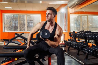 Atletik, yakışıklı, genç, kaslı Avrupalı esmer kızın portresi. Fiziksel egzersiz yapıyor, kol kasları spor salonunda, fotokopi odasında, halterlerle çalışıyor. Siyah tişört ve pantolon giyiyordu. Bakışları ve kasları.