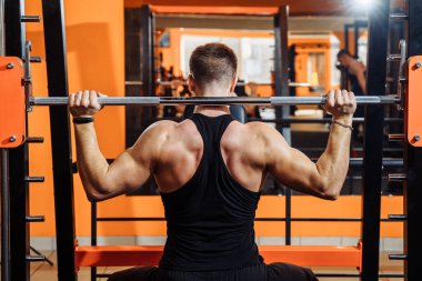 Ortalama plan, geriye bakış. Siyah spor kıyafetleri giymiş kaslı bir adam, çıtayı yükseltmek için kaslarını, pazılarını ve pazılarını çalıştırıyor. Spor ve spor. Sağlıklı yaşam tarzı kavramı