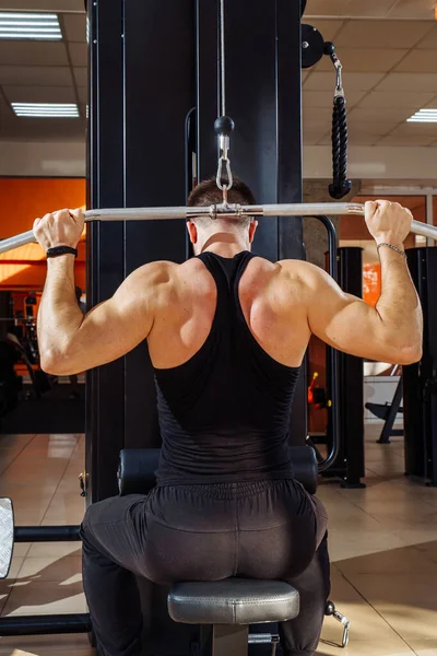 Shoulder pull down machine. Fitness man working out lat pulldown training at gym. Upper body strength exercise for the upper back. Muscular build athlete exercising on pull down weight machine