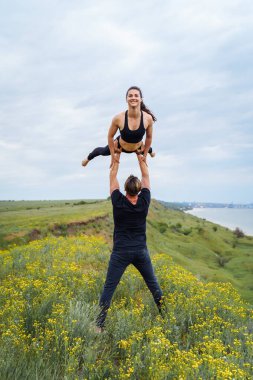 Yaşam tarzı akroyoga ve yoga pozları. Bir çift sporcu ve sporcu Asana pozisyonunda duruyor. Kucağında akrobat bir kız olan kız kollarını uzatarak geriye doğru kavis çizdi. Dışarıdaki insanlardan izole edilmiş.