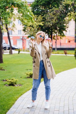 Parkta keyif çatan genç bir kadın, elinde iki lezzetli çörek tutarak eğleniyor. Cilalı, neşeli, mutlu, duygusal, anlamlı, abur cubur, tatlı şekeri, diyet, sağlıklı beslenme, aldatma.