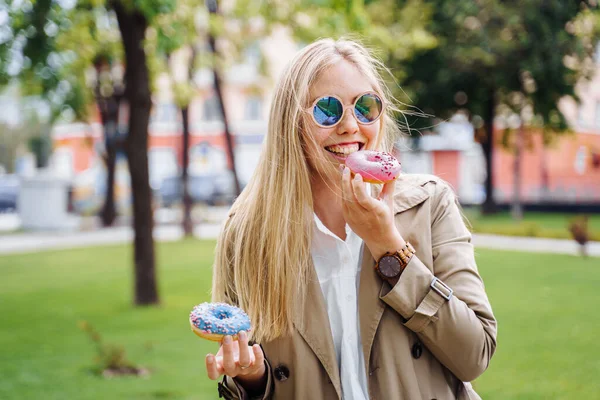 Junk food. Happy delighted woman in casual clothes eating donut with expression of big pleasure, temptation to bite doughnut, appetizing bakery. Sweet tooth,indulgence, gluttony, unhealthy lifestyle