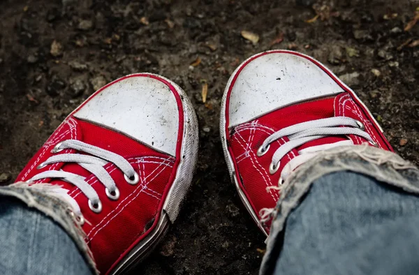 Feet in dirty red sneakers and jeans outdoors. — Stock Photo, Image