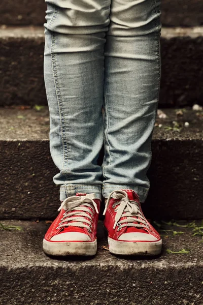 Niña en zapatillas rojas y jeans de pie en las escaleras — Foto de Stock