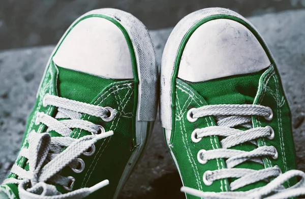 Voeten in vuile groene sneakers en jeans buitenshuis. — Stockfoto