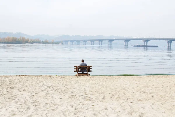 Один человек сидит на скамейке у берега реки . — стоковое фото