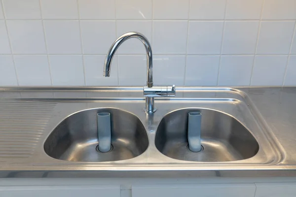 A stainless steel sink in the kitchen with white tiles on the wall