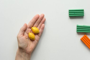 Beyaz arka planda kadın eli üzerinde polimer kilden yapılmış iki el yapımı küçük limon.