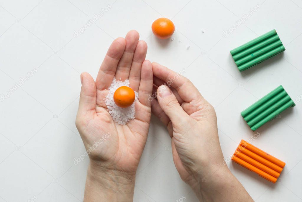 Small orange ball made from polymer clay on woman hand with sea salt to make dents on orange fruit on white background