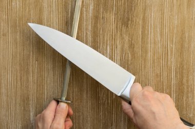 Ahşap arka planda keskinleşen kadın ellerinde bıçak ve bileyici.