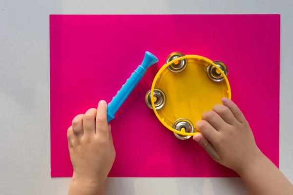 Vista superior de pandereta y manos de niño sosteniendo la tubería sobre el fondo rosa —  Fotos de Stock