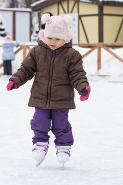 Üç yaşındaki beyaz çocuğun kışın paten sahasında paten kayması ön planda.