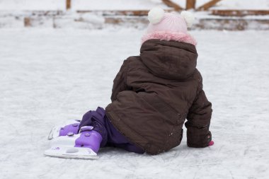 Üç yaşındaki beyaz bir çocuğun kışın paten kayarak paten sahasında oturması.