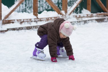 Üç yaşındaki beyaz çocuk kışın paten kayarak paten sahasına düştükten sonra ayağa kalkıyor.