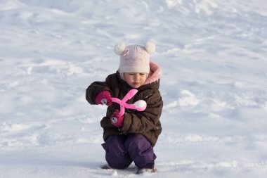 Üç yaşında beyaz bir çocuk kış parkında özel oyuncaklarla kartopu yapıyor.
