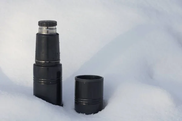 Thermos and cup on snow drift in the winter park — Stock Photo, Image