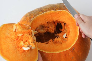 Fırında birkaç dakika geçirdikten sonra tüm balkabağı ve beyaz arka planda bıçakla kesilmiş balkabağının tepesini tutan kadın elleri. Kabağı sert kabukla nasıl keseceğini kavra