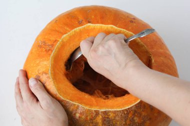 Beyaz arka planda kaşık kullanarak balkabağının içinden tohum çıkaran kadın elleri