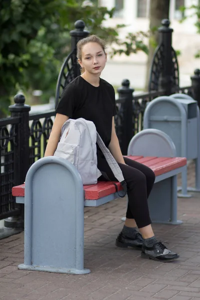 Fiatal nő ül a padon táskával és a kamerába néz — Stock Fotó