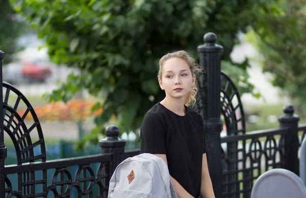 Fiatal nő gondolkodó pillantást ül a padon táskát, és félrenéz — Stock Fotó