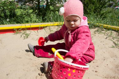 İki yaşındaki çocuk oyun bahçesinde kum havuzunda kum ve kürekle oynuyor.