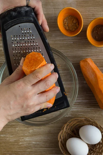 Manos de mujer frotando zanahoria en rallador para pastel de zanahoria en el fondo de madera —  Fotos de Stock
