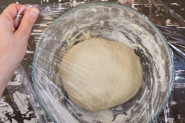 Woman hand cover dough in glass bowl using cling film before proofing