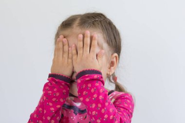 Üç yaşındaki beyaz bir çocuğun portresi beyaz arka planda elleriyle yüzünü kapatıyor.