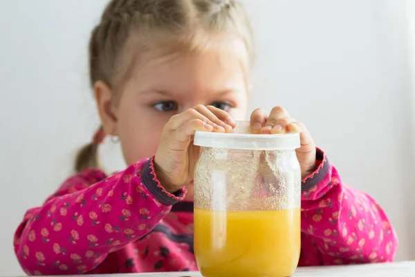 Caucasian child of three years old trying to pull off cover from jar with honey