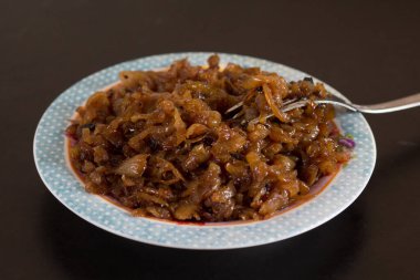 Siyah arka planda çatalla tabakta karamelize edilmiş soğanı kapat