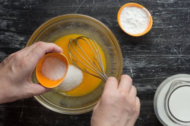 Kadın elinin, siyah arka planda krema yapmak için kaseye şeker koymasının en üst görüntüsü.