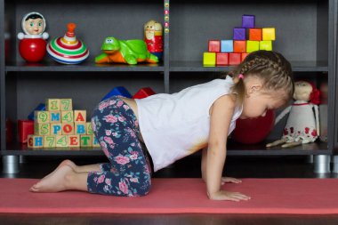 Küçük kız yoga yapıyor kedi ya da inek pozu veriyor geriye doğru eğilip göğsünü açıyor.