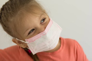 Yüzünde cerrahi maske olan, dört yaşında beyaz bir kızın portresi.