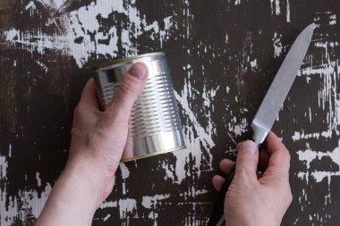 Üst görüşlü kadın kapalı konserve kutusu ve bıçağı ahşap arka planda açmak için tutuyor.