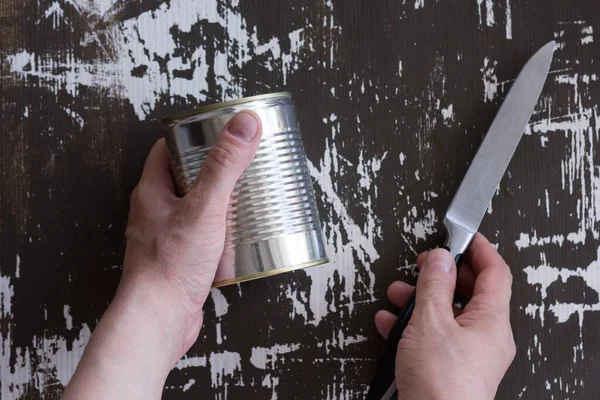 Üst görüşlü kadın kapalı konserve kutusu ve bıçağı ahşap arka planda açmak için tutuyor.
