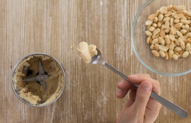 Tahta arka planda öğütücüden yapılmış ev yapımı fıstık ezmeli kaşık tutan kadının üst görüntüsü.