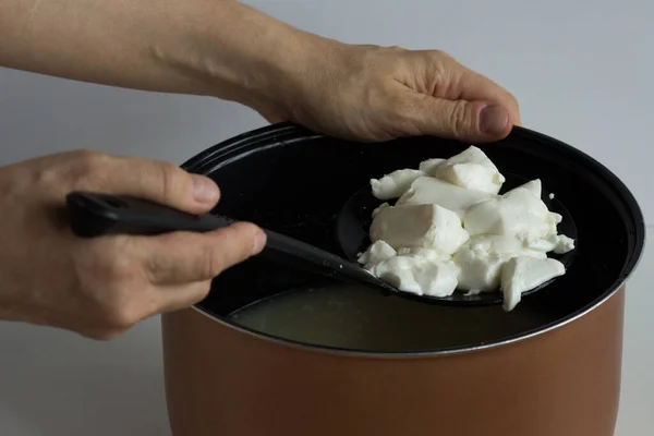 Woman hand holding skimmer with mess of fermented cheese or cottage cheese or greek yogurt taking it from pan to put on the waffle towel or to form — Stock Photo, Image