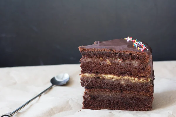 Pedazo de pastel de chocolate en capas y cuchara en el papel artesanal — Foto de Stock