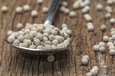 Tahta arka planda kaşıkta beyaz biberleri yakın..