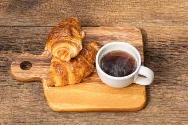 Tahta zemin üzerinde kruvasan olan beyaz bir fincan kahve..