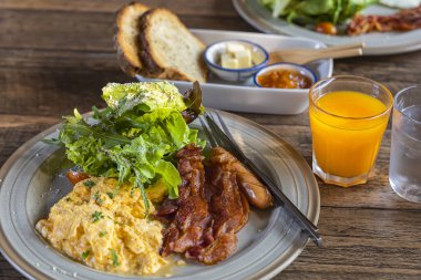 İngiliz kahvaltısı çırpılmış yumurta, pastırma, sebze, portakal suyu ahşap masada..