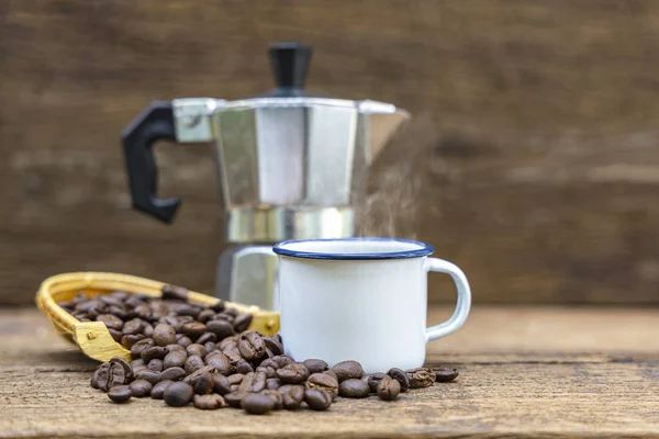 İtalyan kahve demliği (Moka) ve ahşap sehpanın üzerinde kahve çekirdekleri olan beyaz teneke bir kahve..