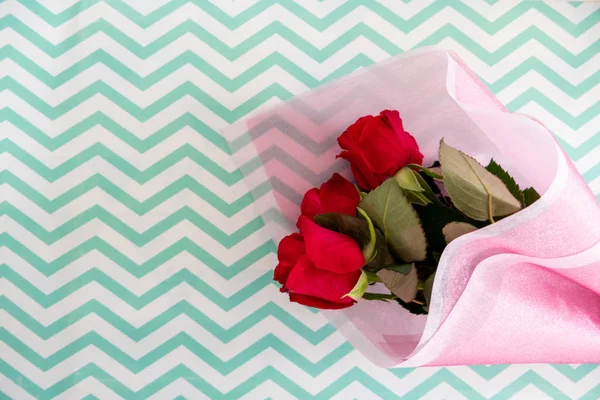 Strauß roter Rosen in rosa Papier auf zickzackigem Hintergrund — Stockfoto
