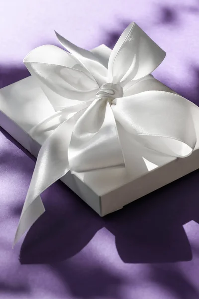 Luksusowe wakacje biały prezent pudełko z jedwabną wstążką i łuk na fioletowym — Zdjęcie stockowe
