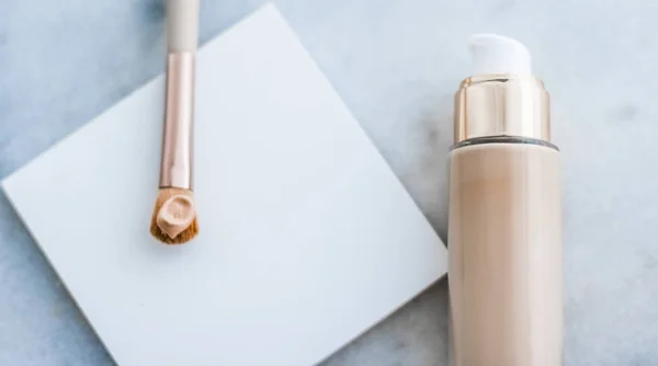 Makeup foundation bottle and contouring brush on marble, make-up