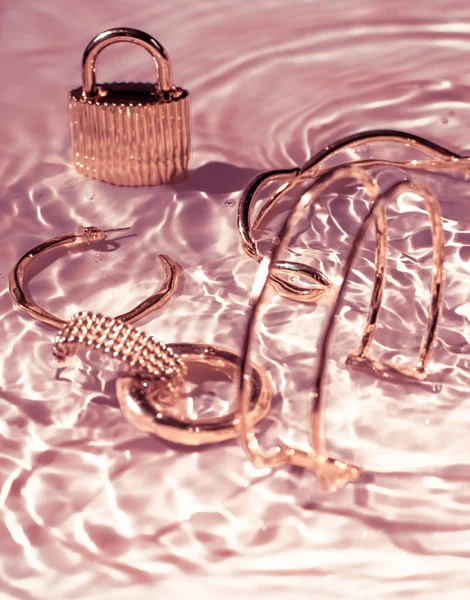 Rose gold bracelets, earrings, rings, jewelery on pink water bac