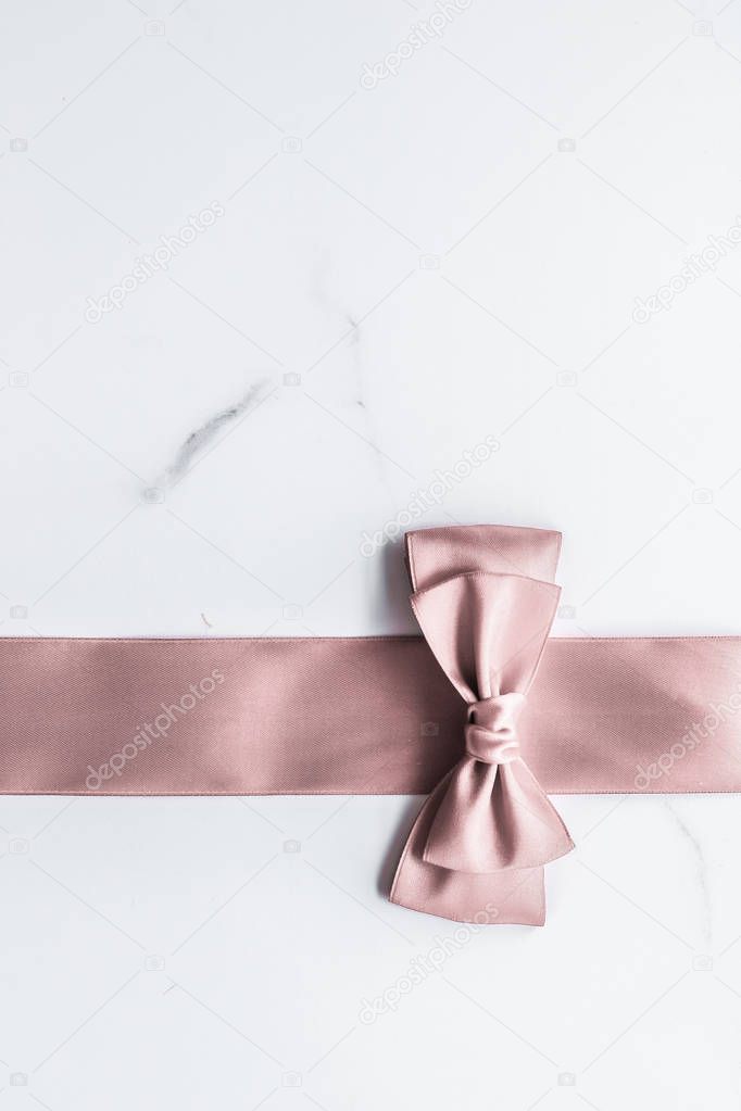 Beige silk ribbon and bow on marble background, glamour present 