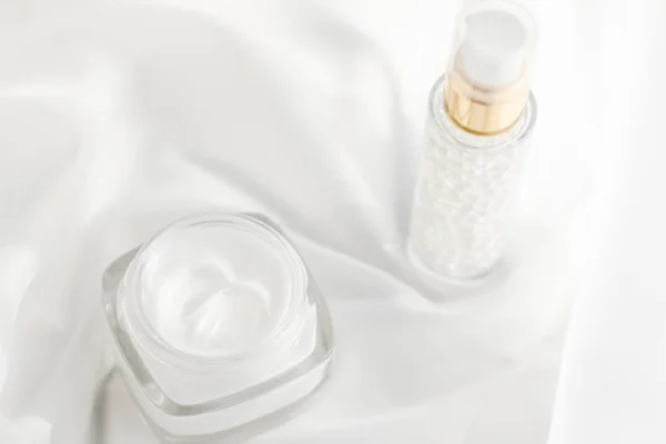 Gezicht crème moisturizer pot en serum gel op witte zijde, huid auto — Stockfoto